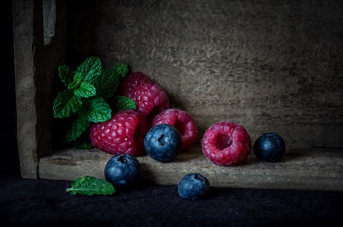 Raspberries and blueberries with mint leaves in a wooden crate