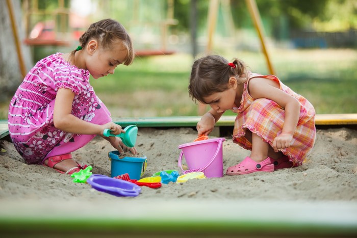 Two little girls playing with toys in a sandbox