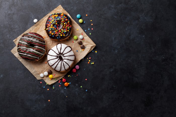 Three donuts with sprinkles and candy on a dark surface
