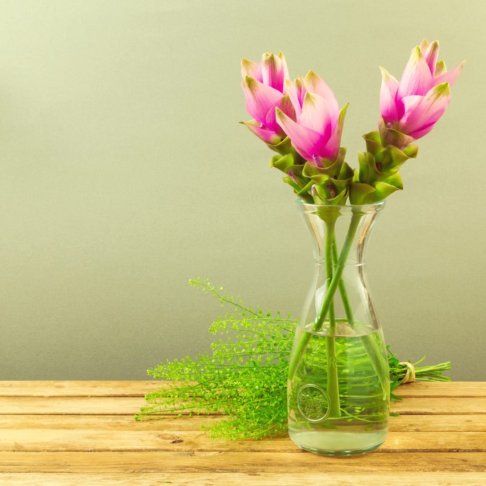 Three pink flowers in a vase with greenery
