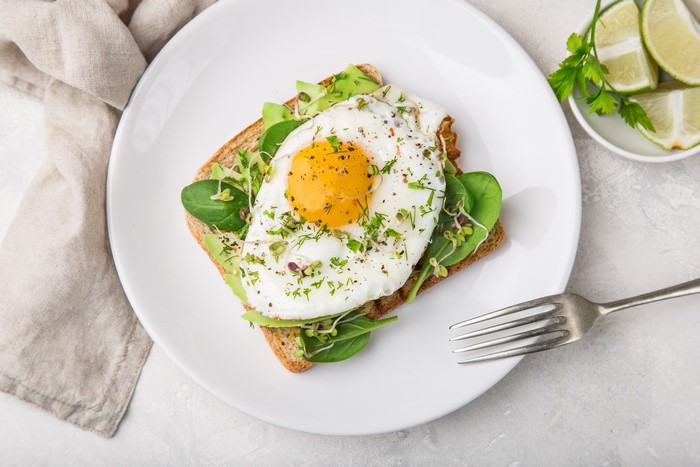 Fried egg on toast with avocado and greens