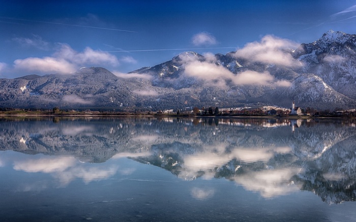 Snow-capped mountains reflected in a calm lake with a village
