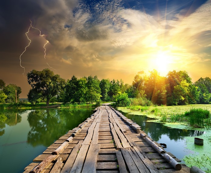 Wooden bridge over water with lightning and sunset