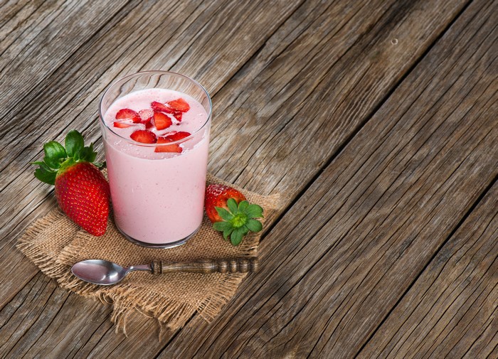 Strawberry smoothie in a glass with strawberries and spoon on wood planks
