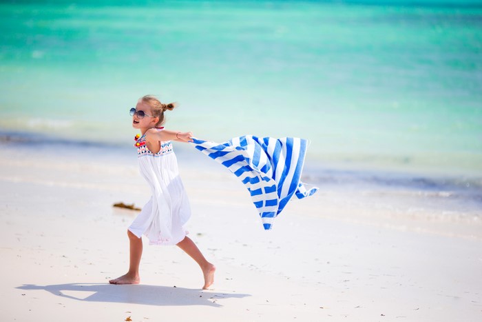 Little girl in dress and sunglasses with towel on beach