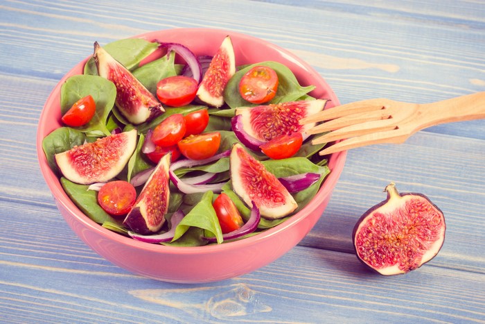 Salad with figs, tomatoes, and spinach on wooden planks