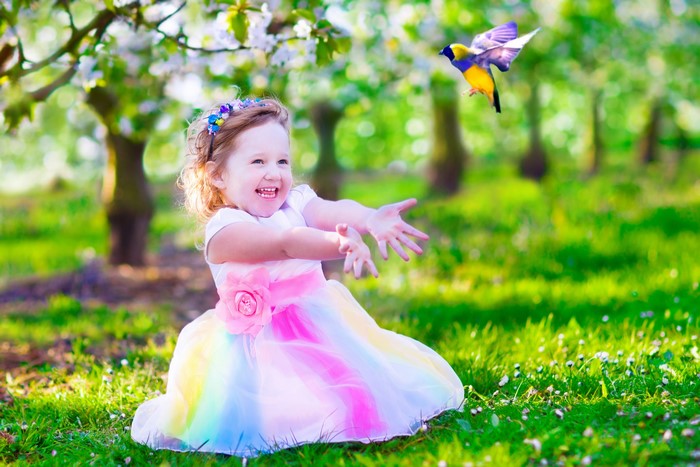 Little girl in rainbow dress reaching for a bird