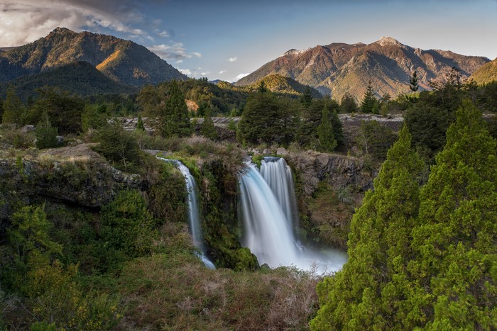 Waterfalls cascading down rocky cliffs with mountains in the background