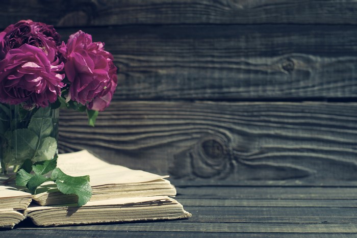 Purple roses and old books on a wooden background