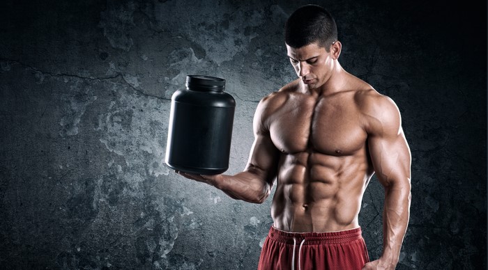 Muscular man holding a black supplement container