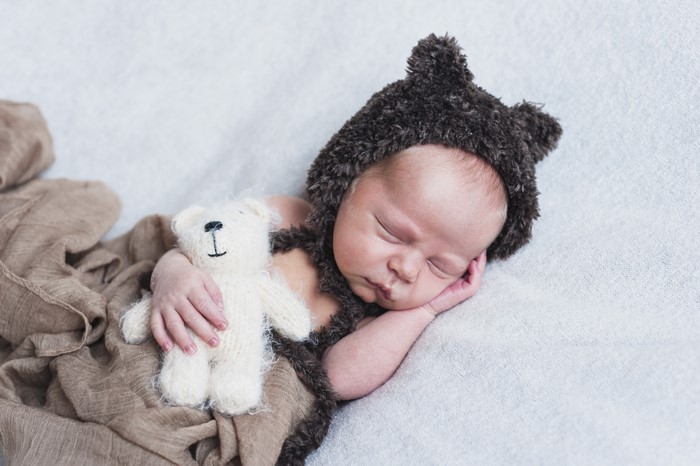 Newborn baby sleeping with teddy bear and winter hat