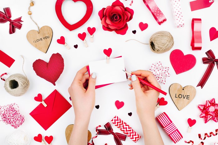 Valentine's Day flat lay with hands writing a card