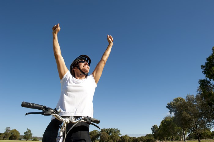 Woman on bicycle with arms raised in celebration