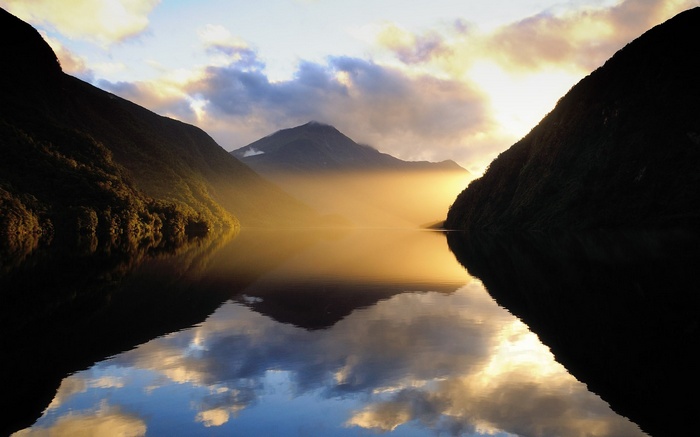 Misty mountains reflected in a calm lake at sunrise