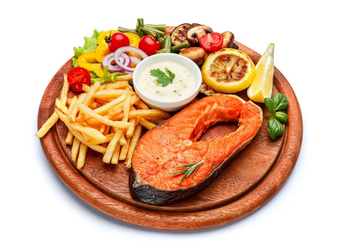 Salmon steak with french fries and vegetables on a cutting board