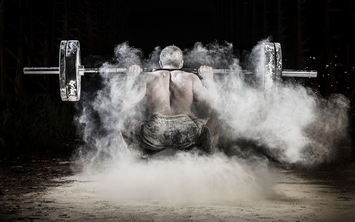 Man performing a squat with a barbell surrounded by chalk dust