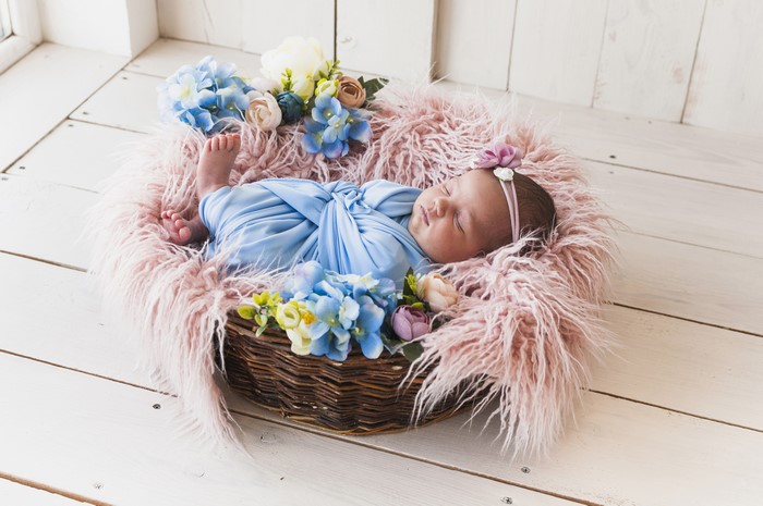 Newborn baby sleeping in a wicker basket with flowers