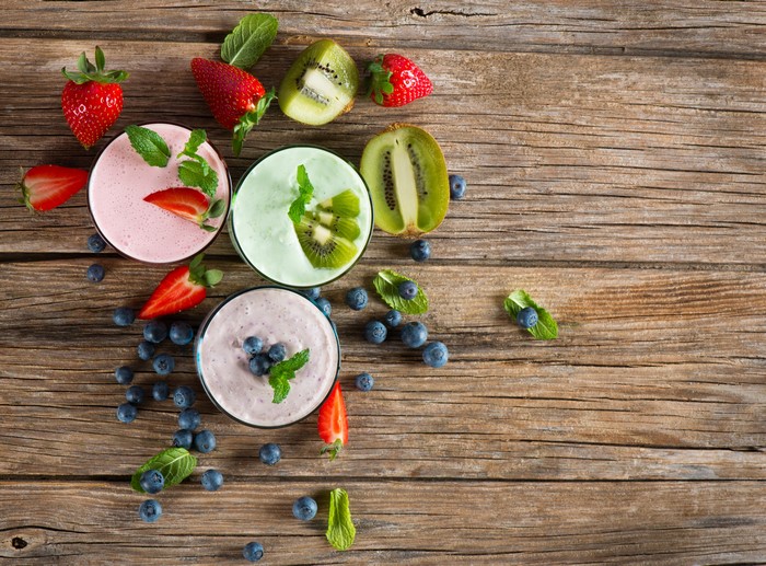 Three fruit smoothies with strawberries, blueberries, and kiwi on wood