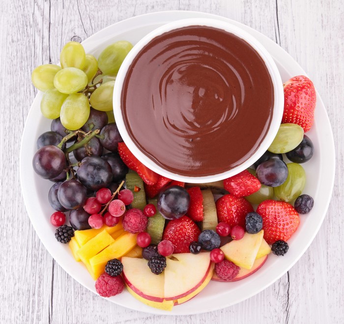 Chocolate fondue with assorted fruits on a white plate