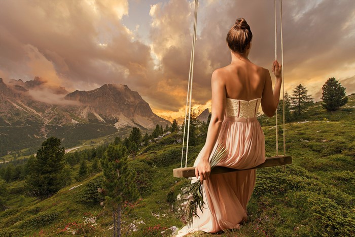 Woman on swing in mountains at sunset