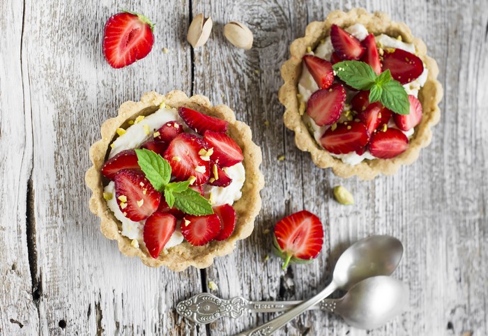 Strawberry tarts with pistachios and mint on wood planks