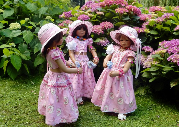 Three dolls in pink dresses and hats in a garden
