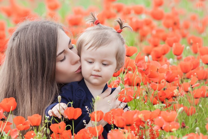 Mother kissing daughter in poppy field