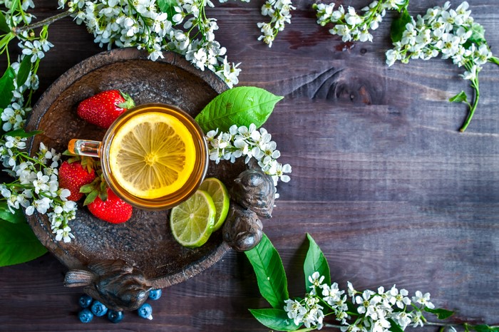 Tea with strawberries, lemon, and lime on a wooden table with flowers
