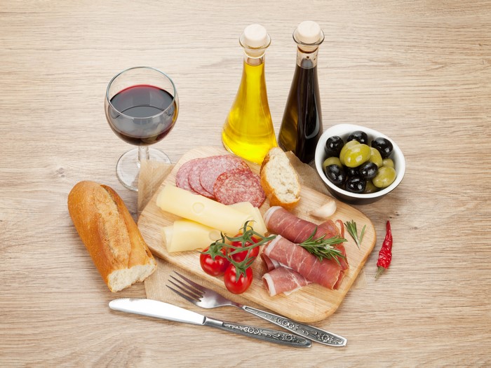 Charcuterie board with wine, cheese, ham, sausage, olives, and bread