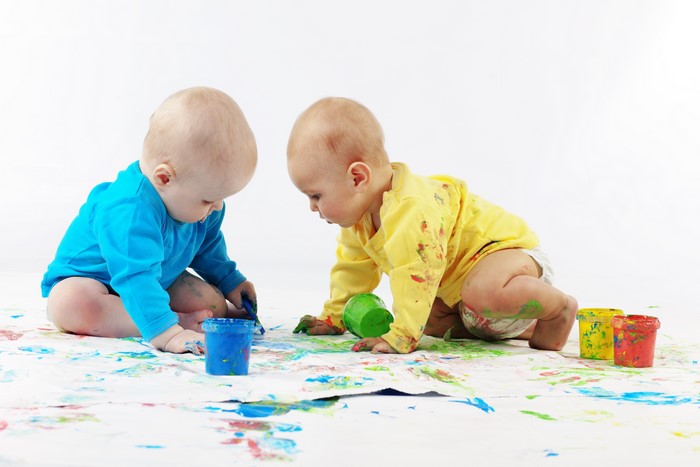Two babies painting with colorful paints