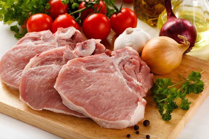 Raw pork chops with vegetables on a cutting board