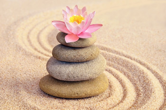 Zen stones stacked with a pink lotus flower on sand
