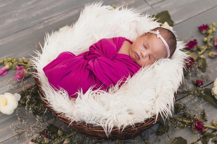 Newborn baby sleeping in a wicker basket with flowers