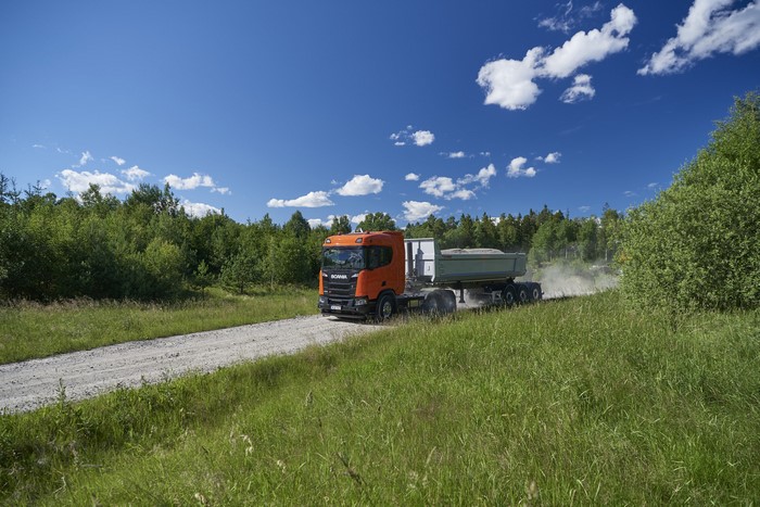 Orange Scania dump truck driving on a dirt road