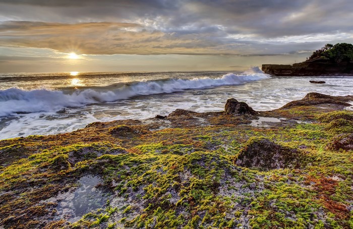 Sunset over the ocean with waves crashing on rocky shore