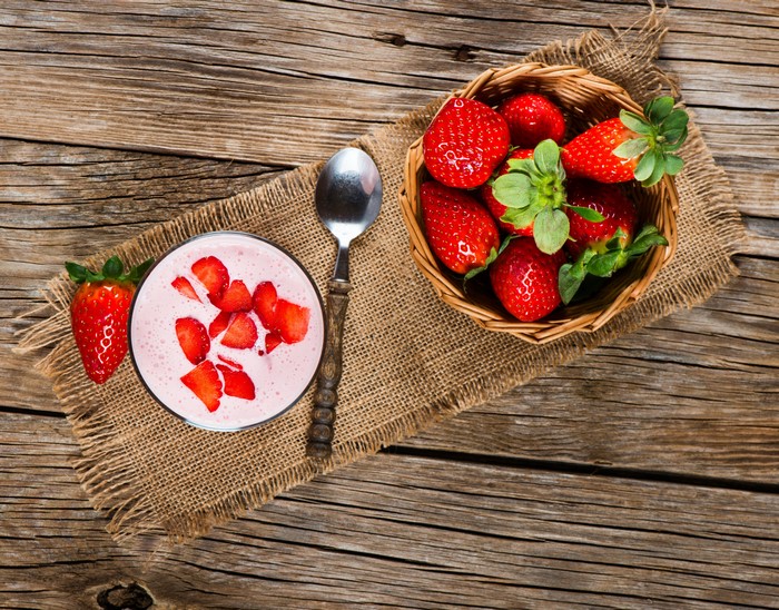 Strawberry yogurt in a glass with a spoon and basket of strawberries on wood