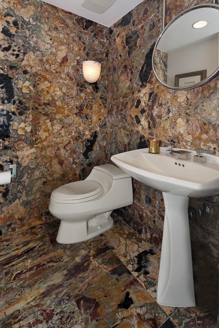 Bathroom with marble walls and floor, toilet, and sink