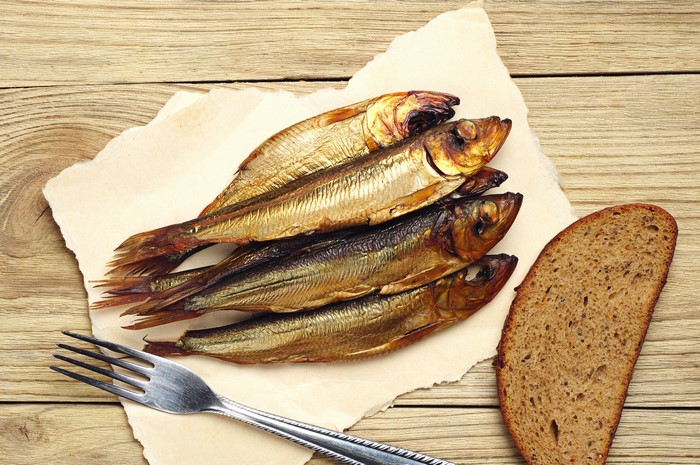 Smoked fish with bread and fork on wood