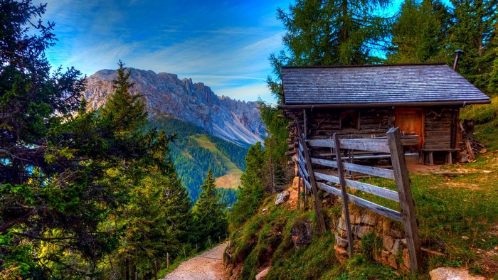 Wooden cabin on a mountain path with Alps in the background