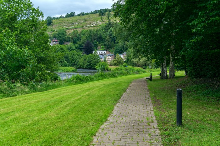 Path along a river with houses on a hill in Laroche, Belgium
