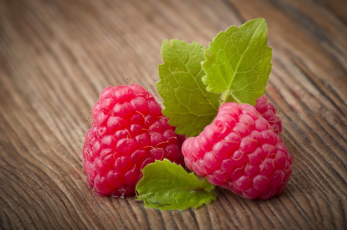 Raspberries with green leaves on a wooden surface