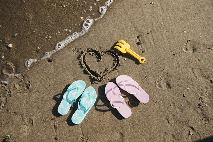 Heart drawn in sand with flip-flops and rake