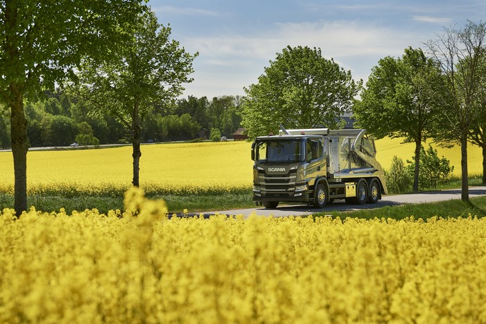 Scania truck driving through a field of yellow flowers
