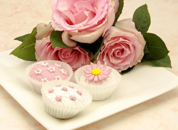 Pink roses and decorated cupcakes on a white plate