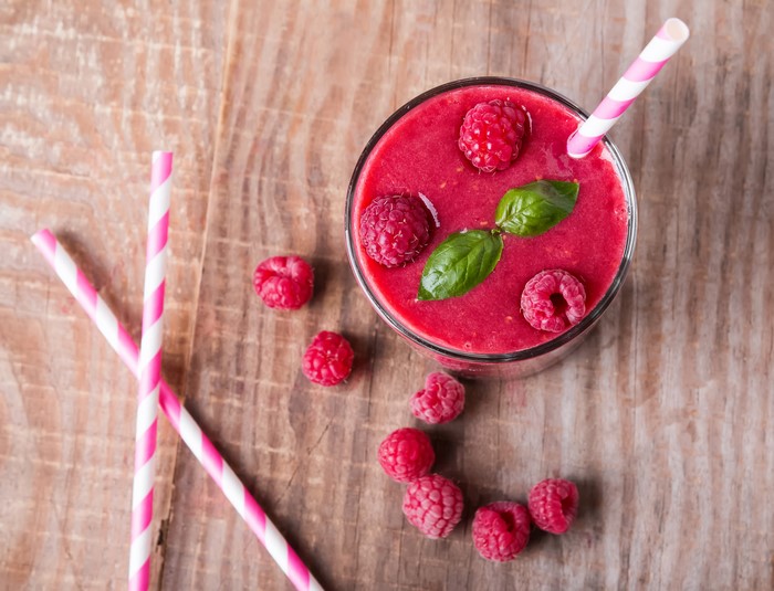 Raspberry smoothie with raspberries and straws on wood