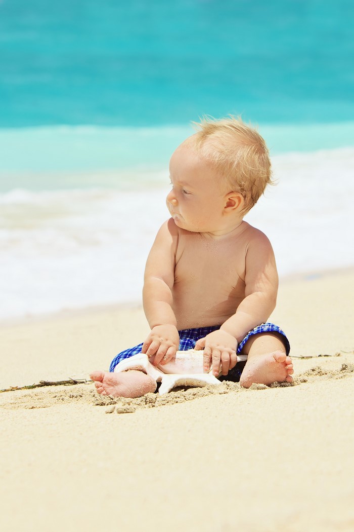 Baby sitting on a sandy beach with a seashell