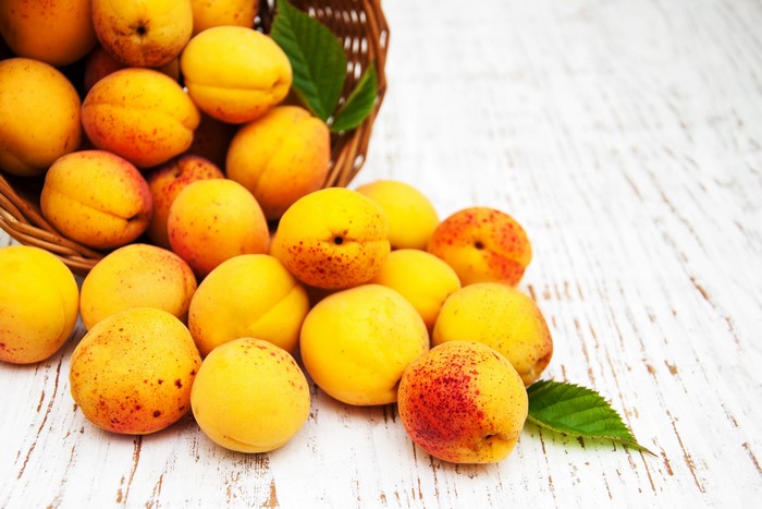 Apricots spilling from a basket onto a wooden surface