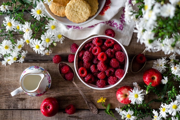 Raspberries, apples, cookies, and flowers on a wooden table
