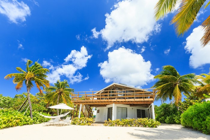 Beach house with palm trees and hammock under blue sky