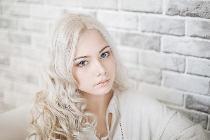 Blonde girl with blue eyes in front of a brick wall